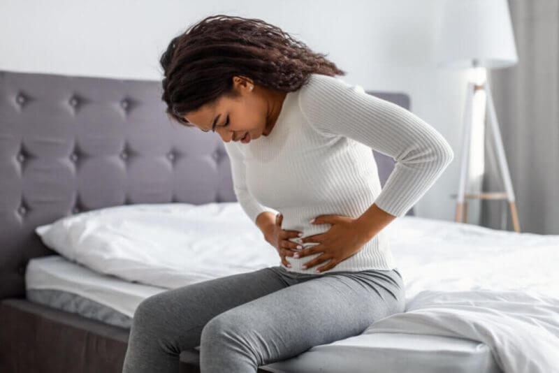 Mulher com as mãos na barriga demonstrando que está com dor