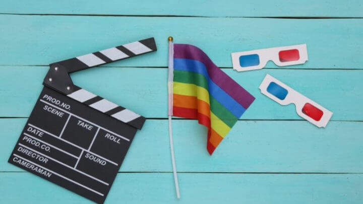 Bandeira do arco-íris LGBT com óculos 3D, claquete de filme sobre fundo azul de madeira.