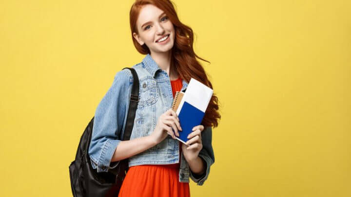 Mulher sorrindo com mochila nas costas e segurando um passaporte