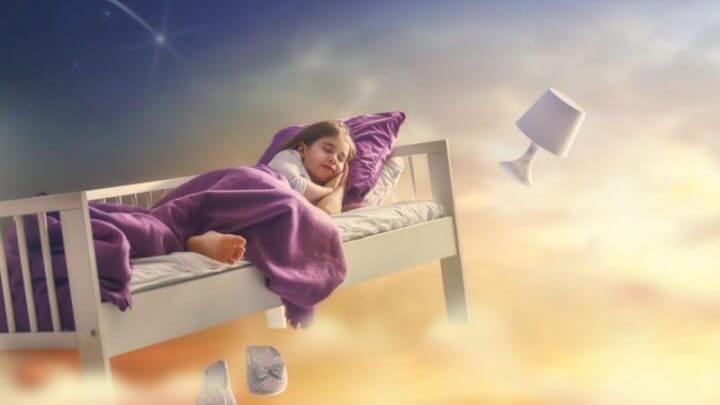 Menina dormindo em sua cama e viajando pelo céu; conceito de sonho