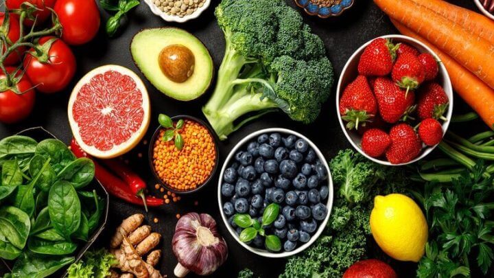 Mesa com brócolis, abacate, laranja, morango e outras frutas espalhadas