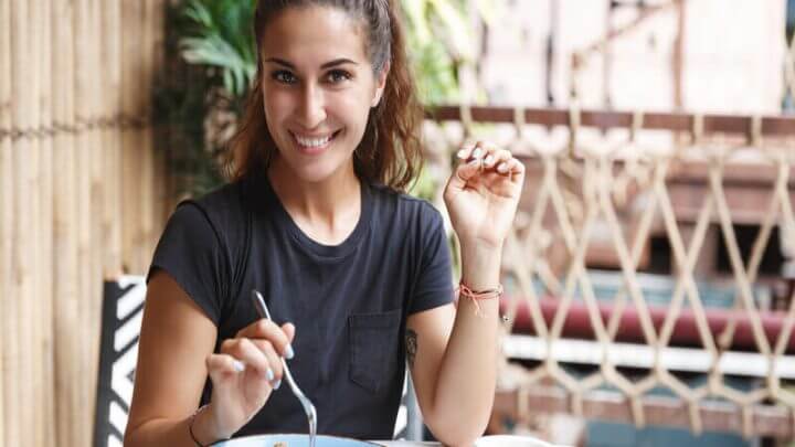Mulher de blusa preta sorrindo comendo em um restaurante