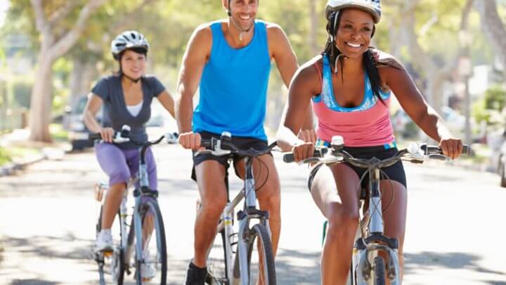 Três pessoas sorridentes andando de bicicleta com capacete.
