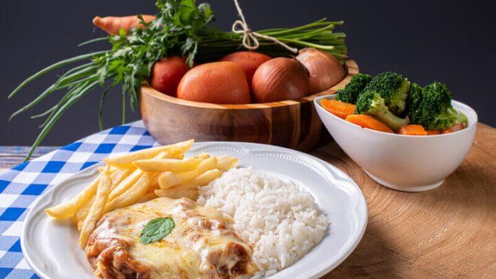 Bife à parmegiana em prato branco com arroz e batata frita