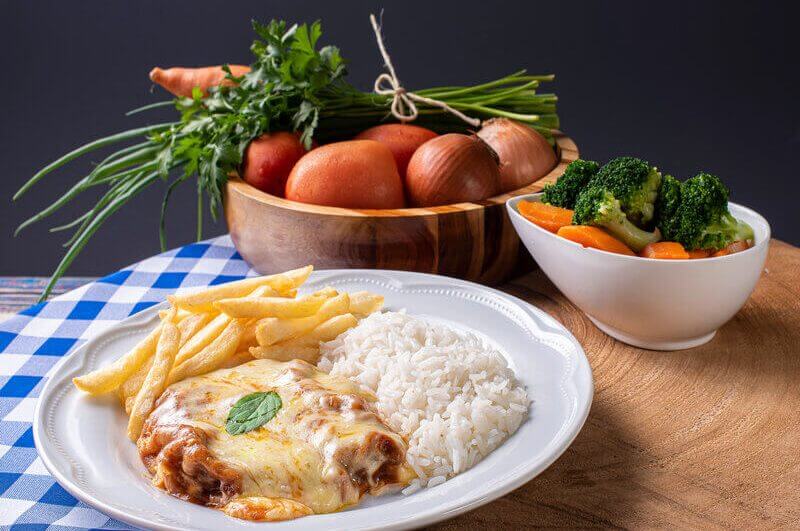 Bife à parmegiana em prato branco com arroz e batata frita