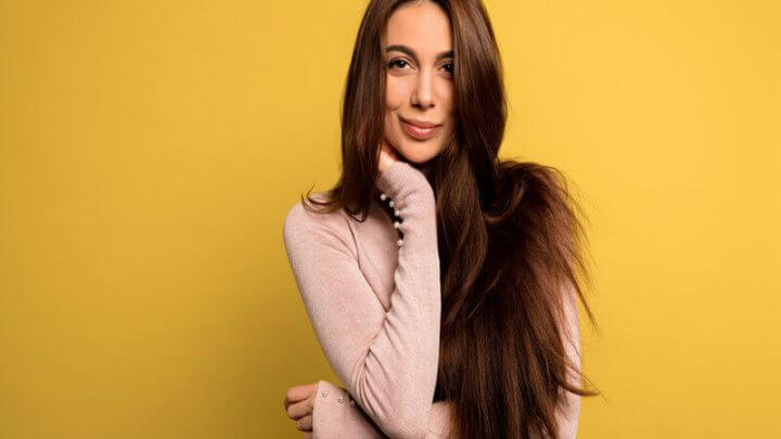 Mulher com cabelos longos usando blusa bege sorrindo em frente a um fundo amarelo