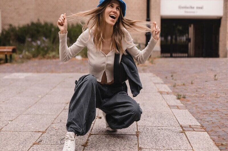 Mulher sorrindo segurando os cabelos e vestindo calça cargo