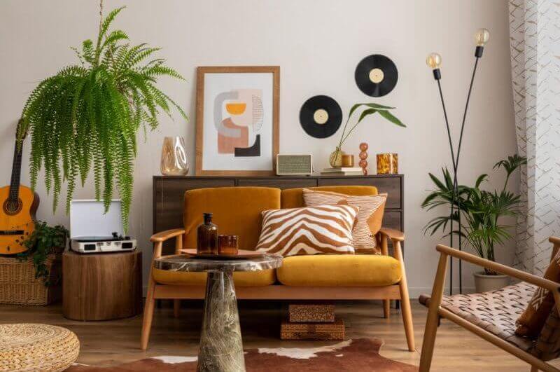 Espaço vintage e aconchegante de sala de jantar com moldura de pôster mock up, sofá amarelo, mesa de centro de madeira, violão, plantas, cômoda, decoração e acessórios pessoais