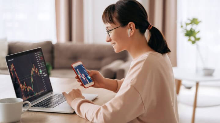 Mulher analisando gráficos financeiros em celular e computador