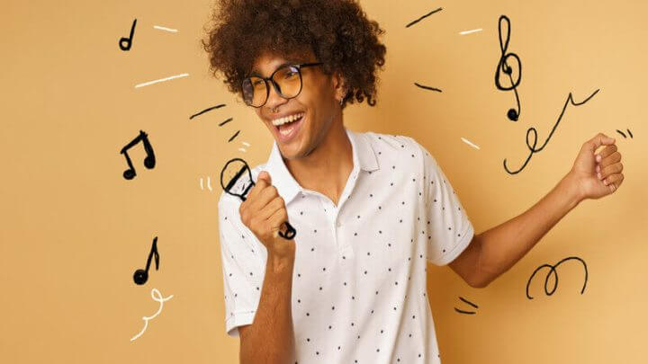 Homem de blusa branca e óculos sorrindo e segurando uma ilustração de microfone
