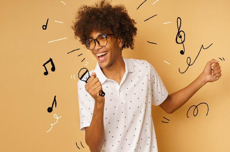 Homem de blusa branca e óculos sorrindo e segurando uma ilustração de microfone