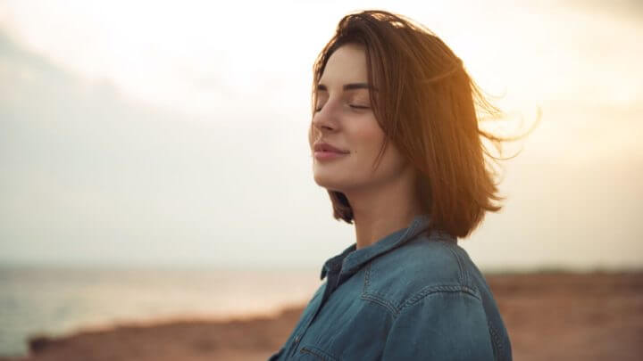 Jovem calma de pé perto do mar com os olhos fechados e expressando relaxamento