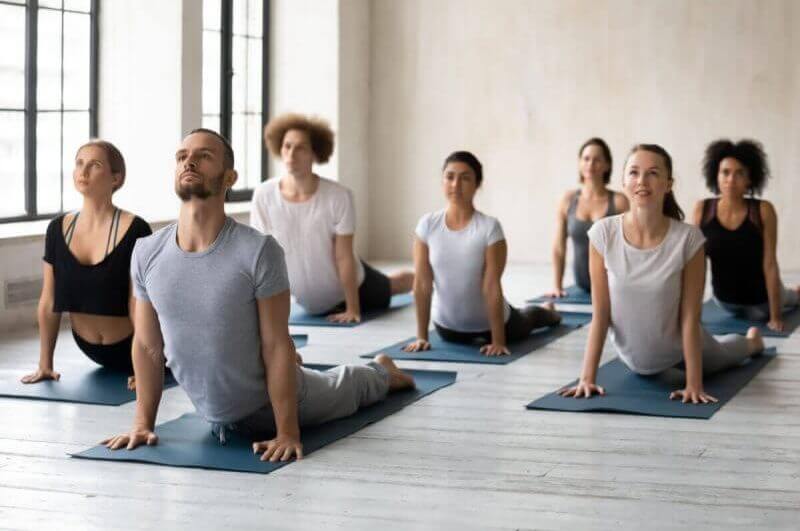 Pessoas em salda fazendo pilates em tapete cinza