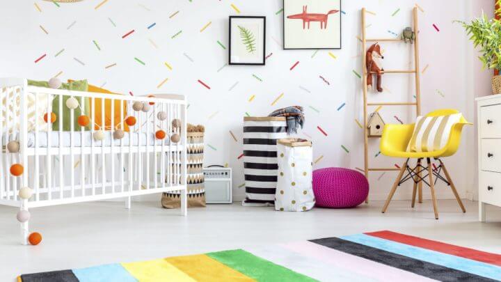 Quarto de bebê com cadeira amarela, berço branco, tapete e decorações muito coloridas.