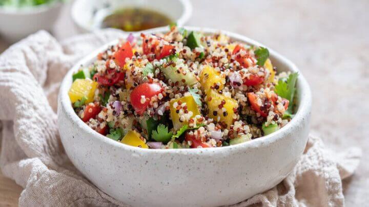 Recipiente branco com quinoa, tomate, pimentão amarelo, pepino e folhas de coentro