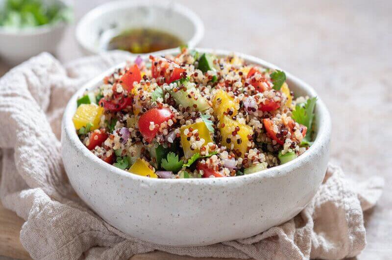 Recipiente branco com quinoa, tomate, pimentão amarelo, pepino e folhas de coentro