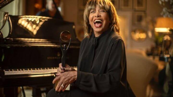 Tina Turner sorrindo ao lado de piano.