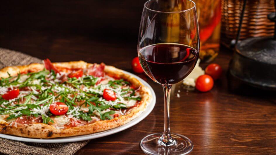 Pizza clássica fina com bordas largas, presunto, tomates-cereja, rúcula, queijo parmesão e vinho tinto.
