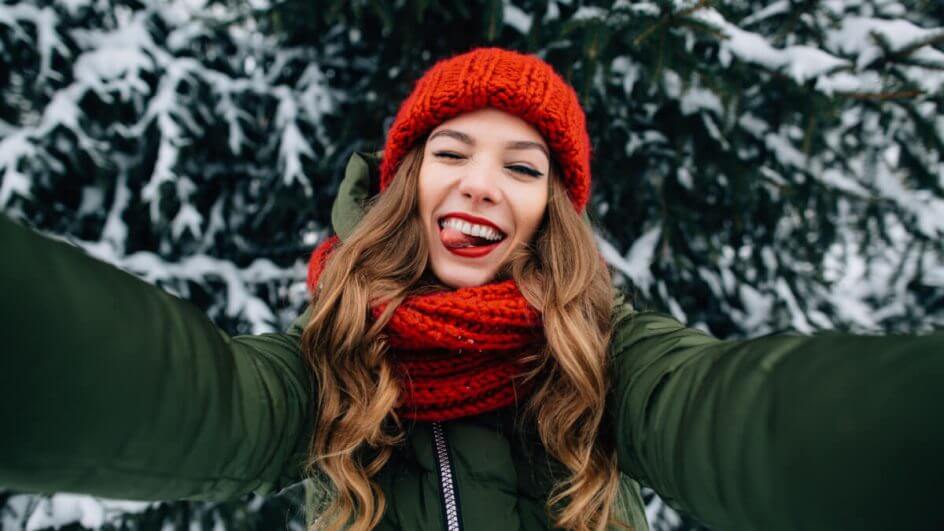Jovem feliz com touca de malha vermelho e cachecol tirando selfie