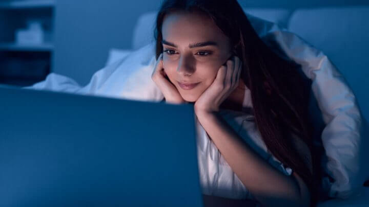 Jovem assistindo a filme em computador durante a noite, com atenção e interesse.