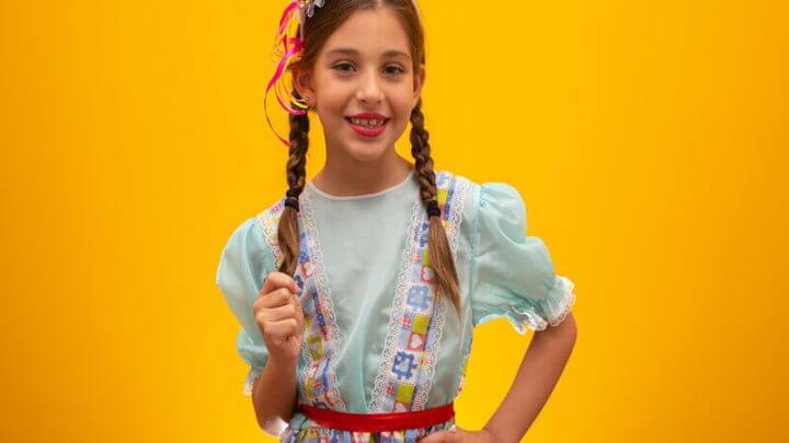 Menina com roupa de festa junina e mini chápeu sorrindo