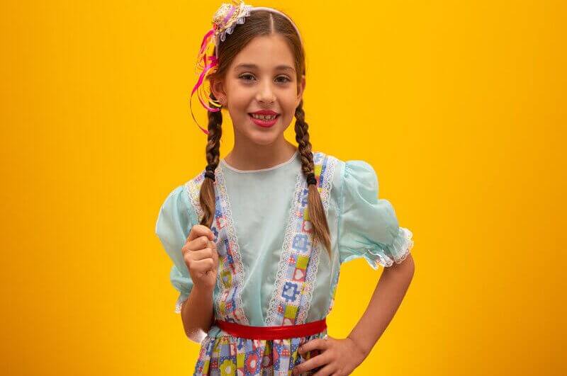 Menina com roupa de festa junina e mini chápeu sorrindo
