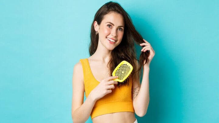 Mulher com blusa amarela penteando os cabelos e sorrindo