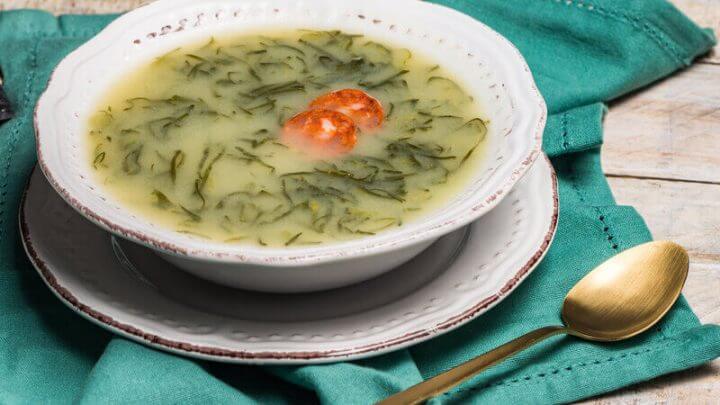 Prato branco com caldo verde em cima de uma mesa de madeira