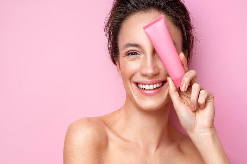 Mulher sorrindo segurando um recipiente rosa em frente ao rosto
