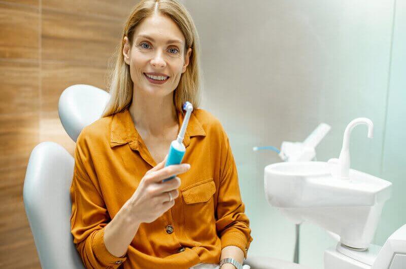 Mulher de blusa laranja sentada, sorrindo e segurando uma escova de dentes