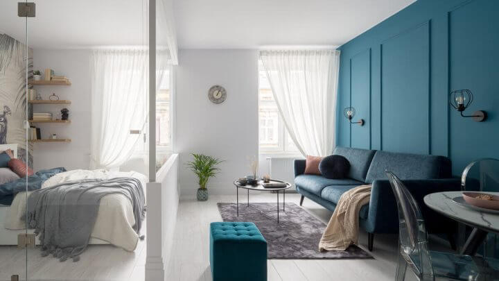 Apartamento com parede e sofá verde, cortina branca e espelhos