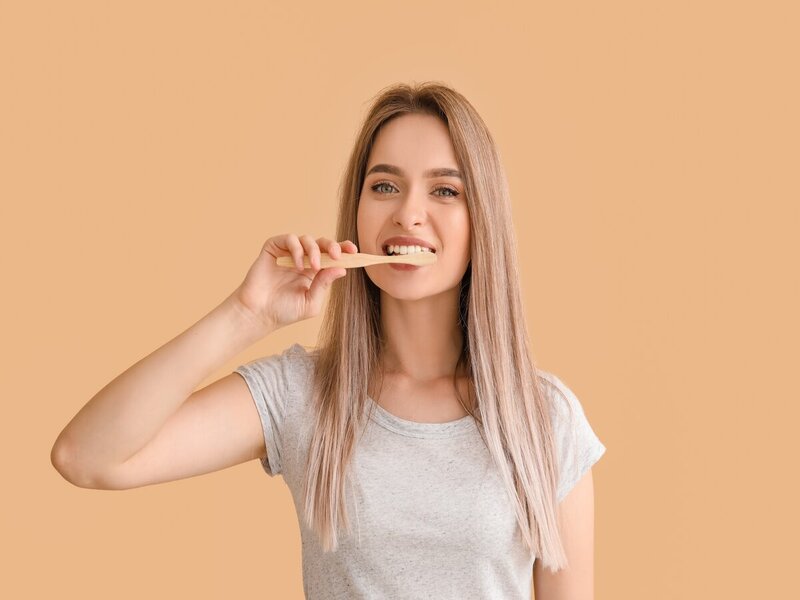 Mulher loira com blusa branca escovando os dentes