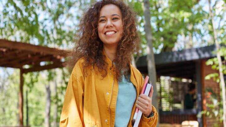 Mulher de blusa amarela sorrindo e segurando livros em um parque