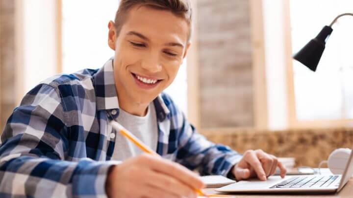Menino de blusa xadrez sentado sorrindo e estudando