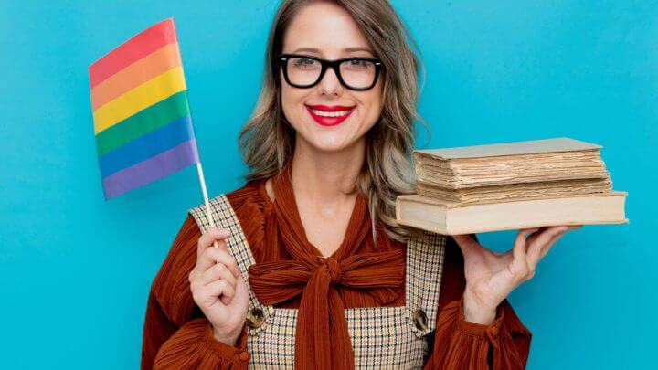 Mulher de óculos segurando livros e bandeira LGBTQIA+