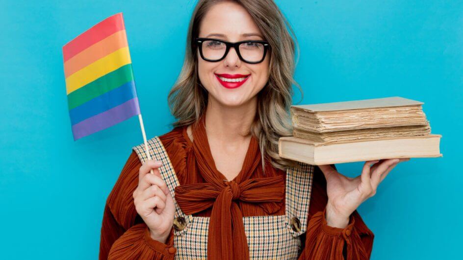 Mulher de óculos segurando livros e bandeira LGBTQIA+