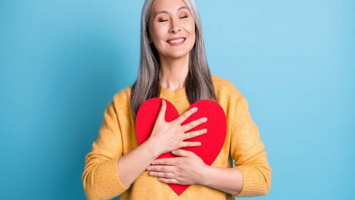 Mulher sorrindo segurando um coração vermelho de papel