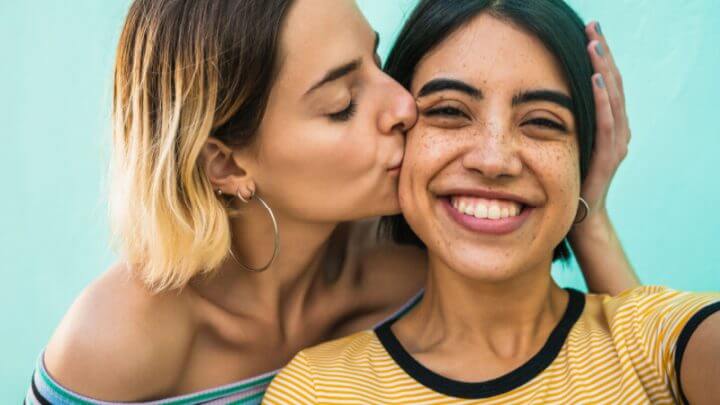 Mulher loira beijando bochecha de mulher morena