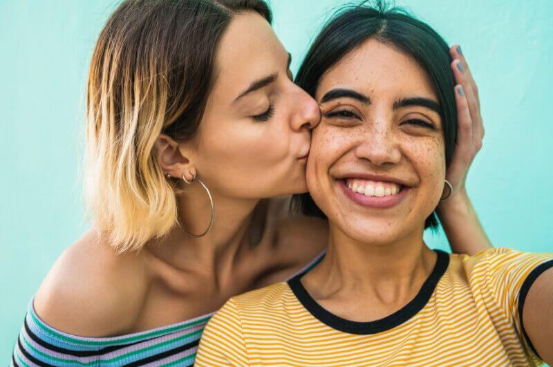 Mulher loira beijando bochecha de mulher morena