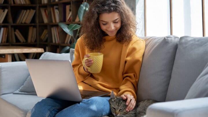 Mulher com notebook no colo fazendo carinho na cabeça do gato