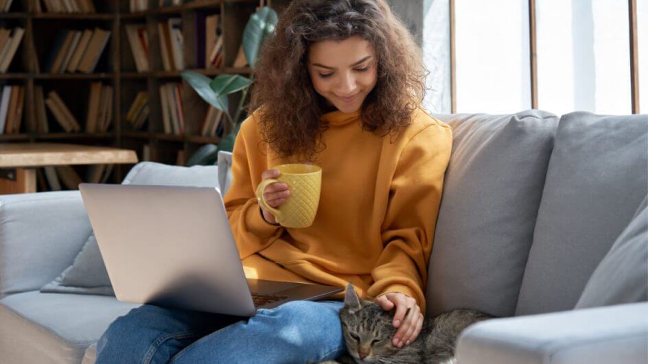 Mulher com notebook no colo fazendo carinho na cabeça do gato