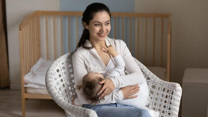 Mulher sentada sorrindo amamentando um bebê