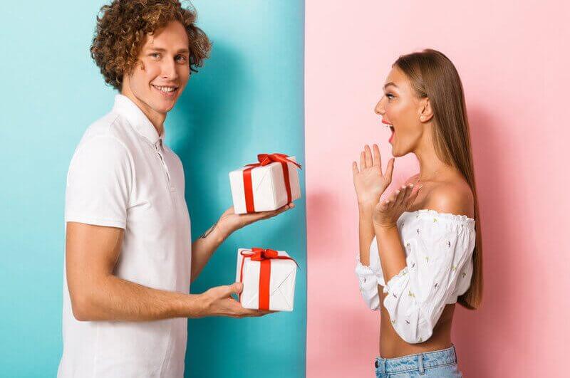 Homem segurando dois presentes e uma mulher surpresa