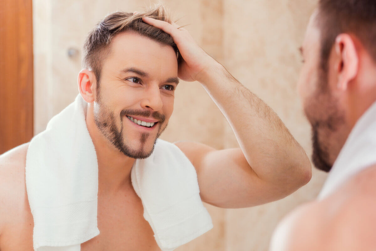 Homem sorrindo com a mão no cabelo em frente a um espelho
