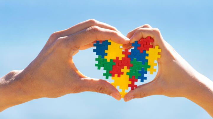 Mãos de criança e adulto segurando um coração colorido, símbolo da conscientização sobre o autismo