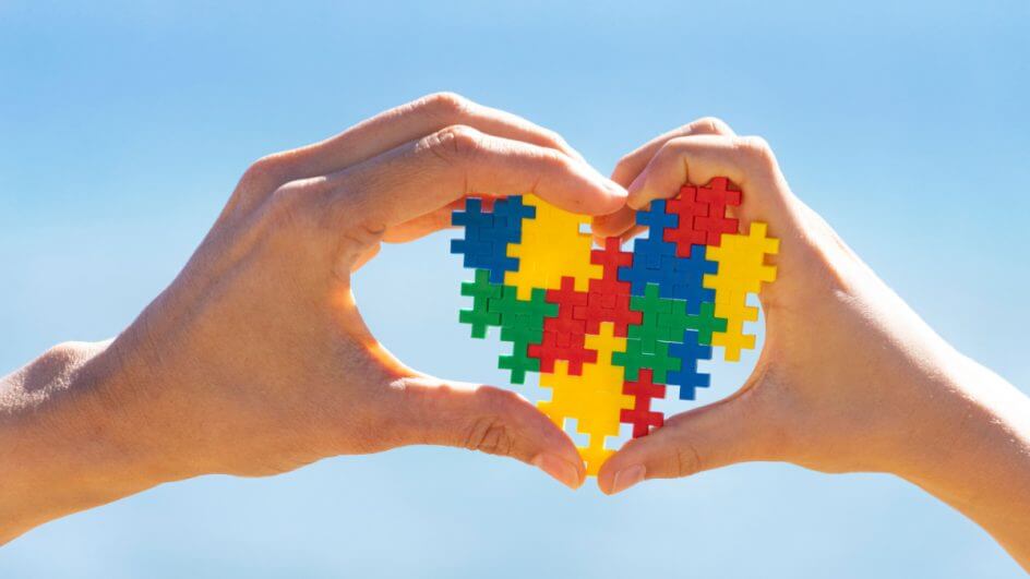 Mãos de criança e adulto segurando um coração colorido, símbolo da conscientização sobre o autismo