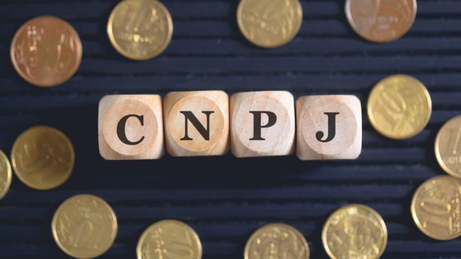 A sigla CNPJ para o Cadastro Nacional de Pessoas Jurídicas escrita em dados de madeira com moedas brasileiras na composição