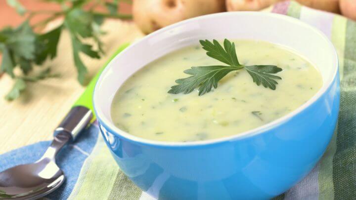 Caldo de batata com ervas em recipiente azul com batatas ao fundo
