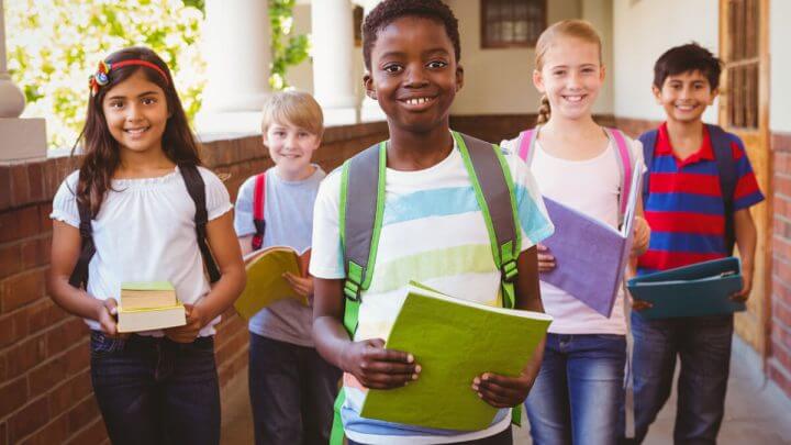 Crianças em uma escola com mochilas nas costas e segurando cadernos