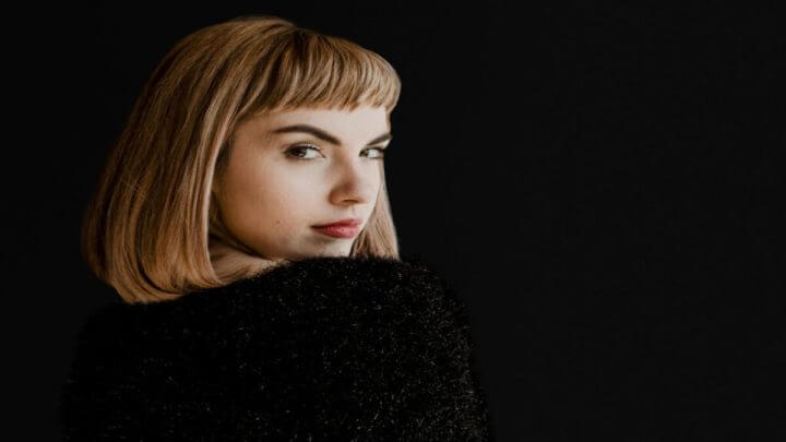 Mulher loira de cabelo curto e roupa preta olhando acima do ombro
